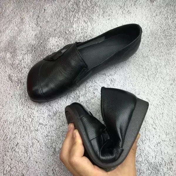 Chaussures noires en cuir souple pour femmes, pliables et confortables, idéales pour le voyage. Design élégant et pratique sur fond texturé gris.
