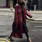 Femme portant un long manteau en cuir rouge, tenue noire élégante, talons aiguilles, marchant en ville. Mode urbaine chic, style automne-hiver.