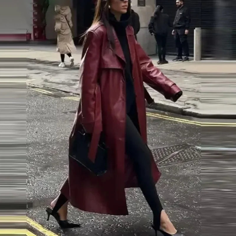 Femme portant un long manteau en cuir rouge, tenue noire élégante, talons aiguilles, marchant en ville. Mode urbaine chic, style automne-hiver.