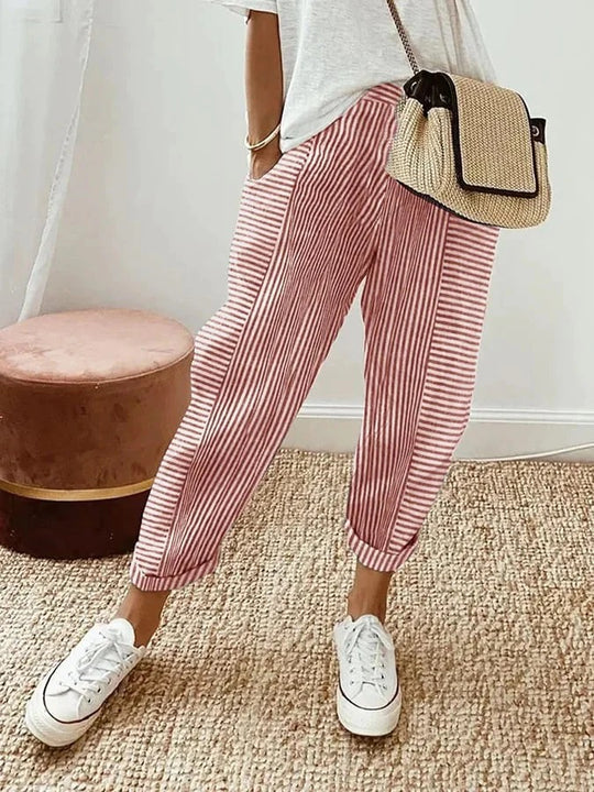 Pantalon rayé rouge et blanc, style décontracté, porté avec un t-shirt blanc, baskets blanches et sac en osier, sur tapis beige.