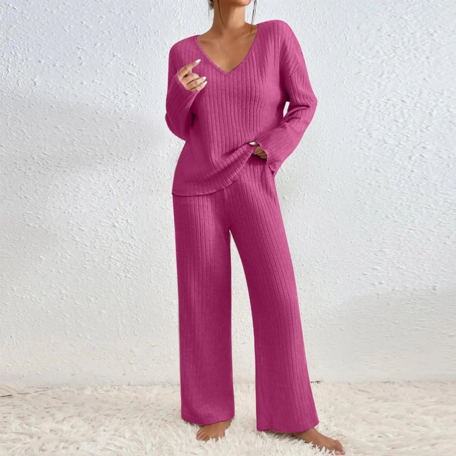 Femme portant un ensemble confortable en tricot rose, composé d'un pull à manches longues et d'un pantalon ample, sur un tapis blanc.