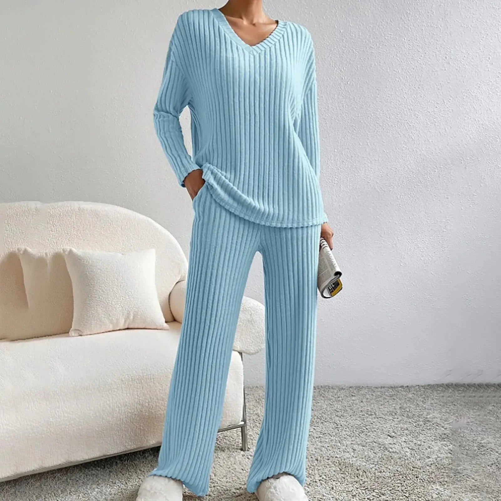 Pyjama femme bleu clair en tricot côtelé, confortable et élégant, avec pantoufles blanches moelleuses, posé dans un salon moderne.