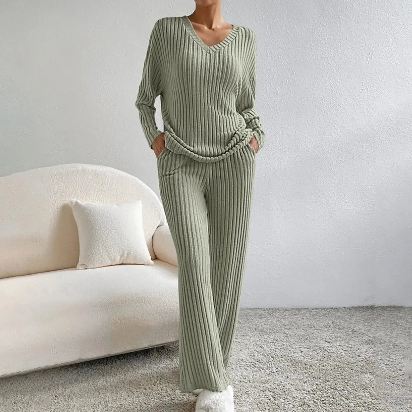 Femme portant un ensemble lounge en tricot vert, confortable et élégant, avec un canapé blanc en arrière-plan. Mode détente automne-hiver.