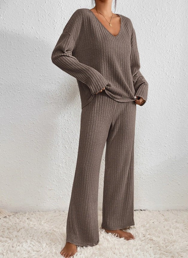 Femme portant un ensemble lounge en tricot marron, pull à col en V et pantalon ample, sur tapis blanc. Mode confortable et élégante.
