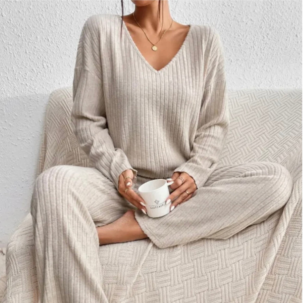 Femme en pyjama beige côtelé, assise sur un canapé, tenant une tasse blanche. Mode détente, confort à la maison, style cocooning élégant.