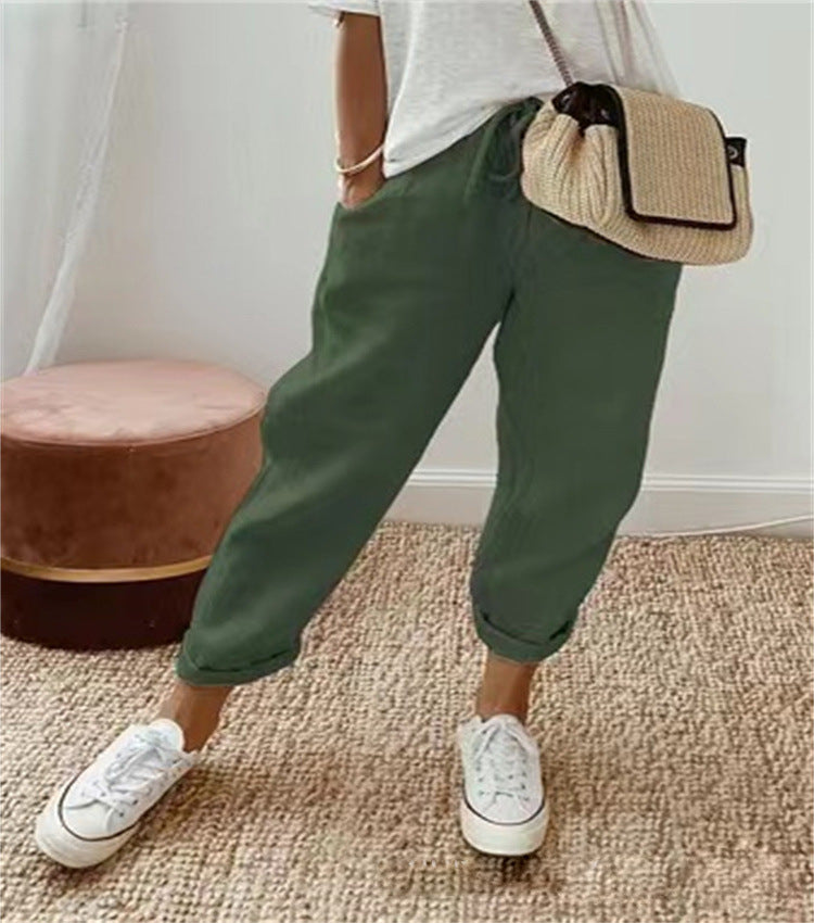 Pantalon vert décontracté pour femme, associé à un t-shirt blanc et des baskets blanches, sac à main en paille, sur fond de tapis beige.