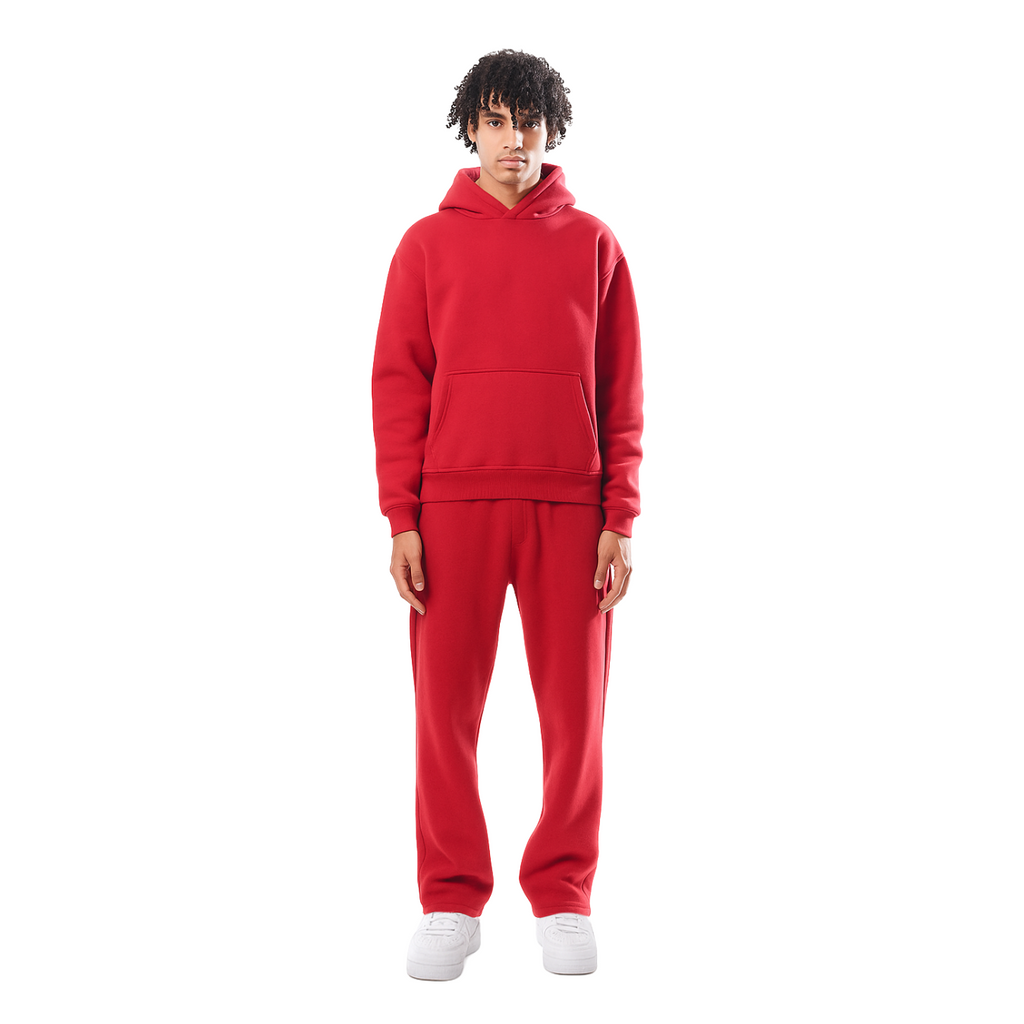 Jeune homme en survêtement rouge, debout, portant un sweat à capuche et un pantalon assorti, sur fond blanc. Mode décontractée, style urbain.