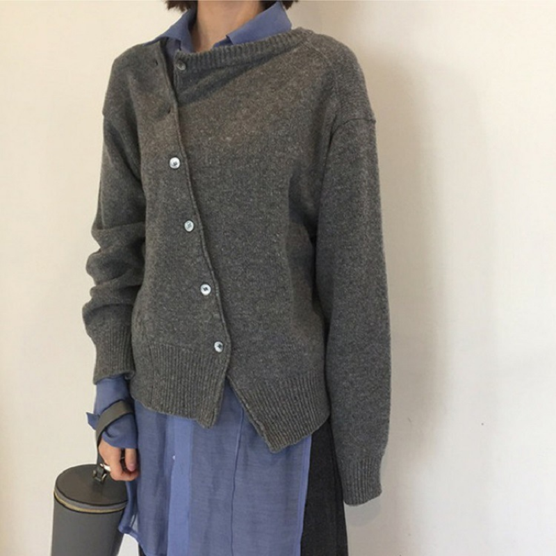 Femme portant un cardigan gris asymétrique sur une chemise bleue, tenant un sac noir. Mode automne, style décontracté, tendance vêtements superposés.