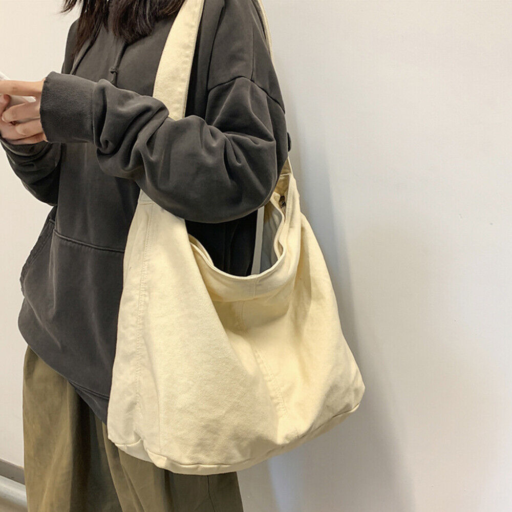 Personne portant un sweat-shirt sombre et un pantalon kaki, tenant un grand sac en toile beige. Mode décontractée, style urbain, accessoire tendance.