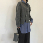 Personne portant un pull gris sur une chemise bleue, tenant un sac à main cylindrique gris. Mode décontractée, style automne-hiver, vêtements superposés.
