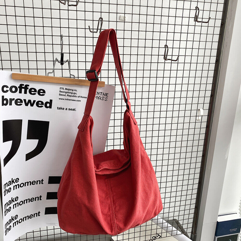 Sac à bandoulière rouge en toile suspendu à un crochet, devant un mur grillagé avec une affiche de café. Accessoire mode tendance et pratique.