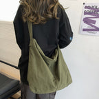 Femme portant un grand sac en toile vert olive, style décontracté, mode urbaine, dos à la caméra, intérieur moderne, lumière naturelle.
