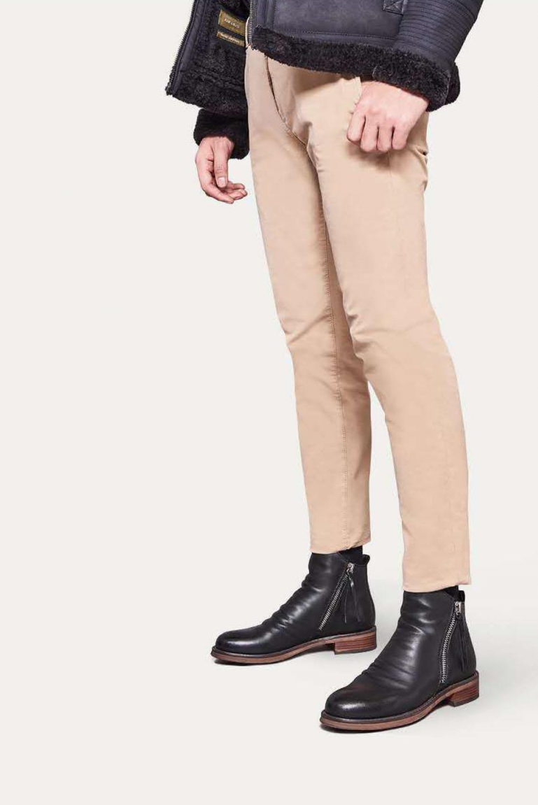 Homme portant un pantalon beige et des bottines en cuir noir avec fermeture éclair, style mode masculine élégante et moderne.