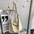 Sac à main en toile beige suspendu devant un fond de grille métallique, avec affiches modernes en noir et blanc. Accessoire mode tendance et minimaliste.