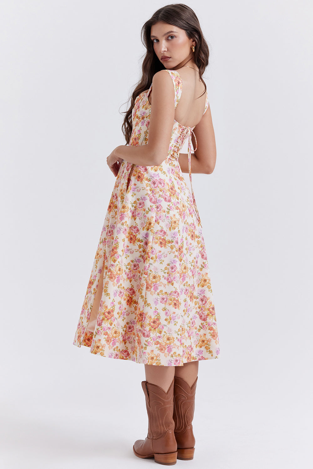 Robe longue à fleurs roses et jaunes, dos nu, portée par une femme avec des bottes marron. Mode féminine, style estival, élégance décontractée.