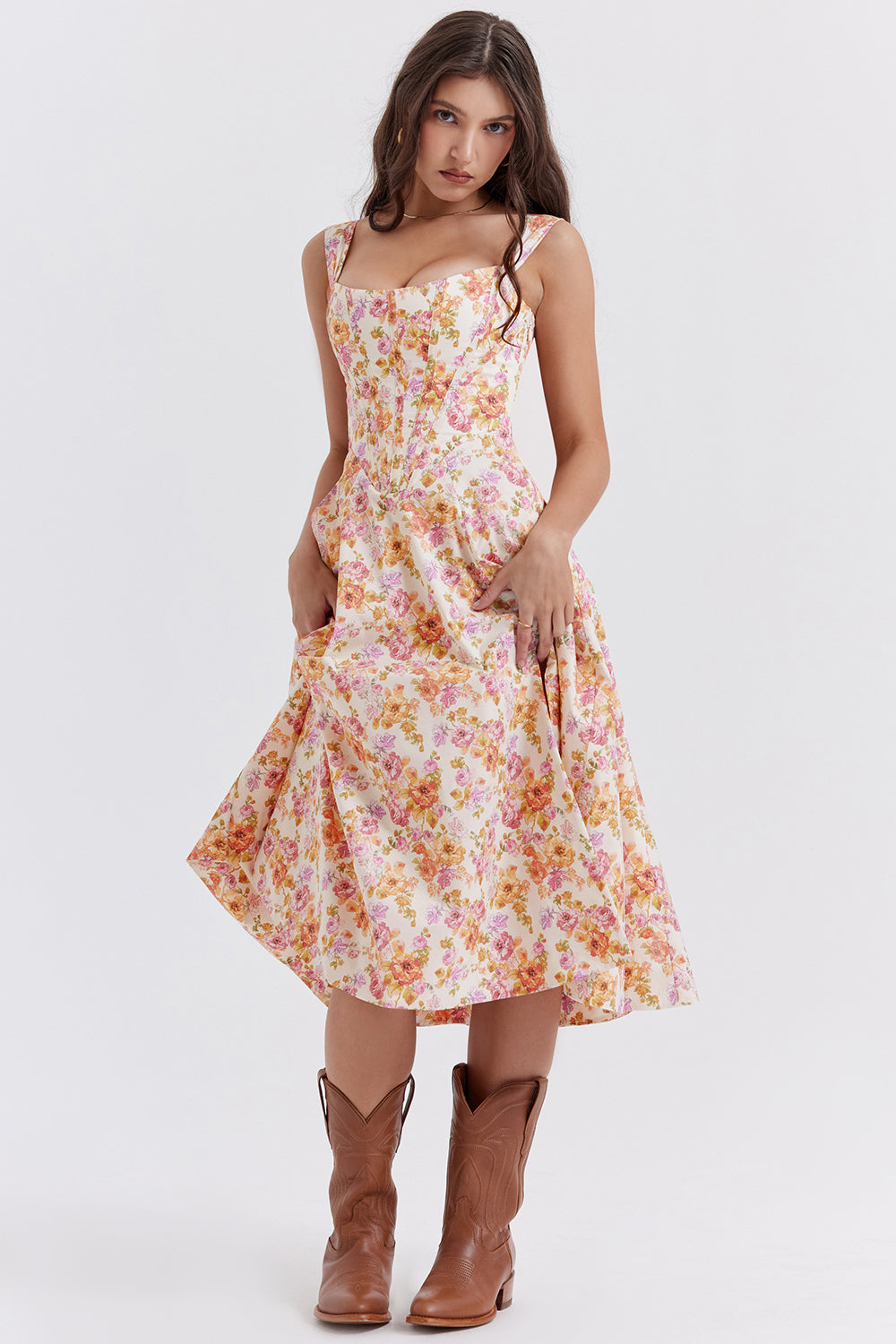 Robe longue à fleurs roses et jaunes, style vintage, portée par une femme avec des bottes marron. Mode féminine élégante et rétro.