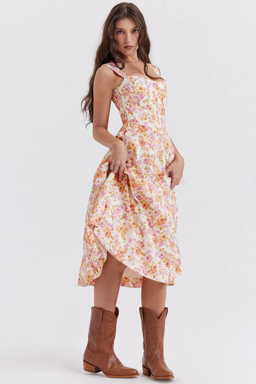 Jeune femme portant une robe à fleurs pastel et des bottes marron, posant debout. Mode féminine, style champêtre, élégance décontractée.