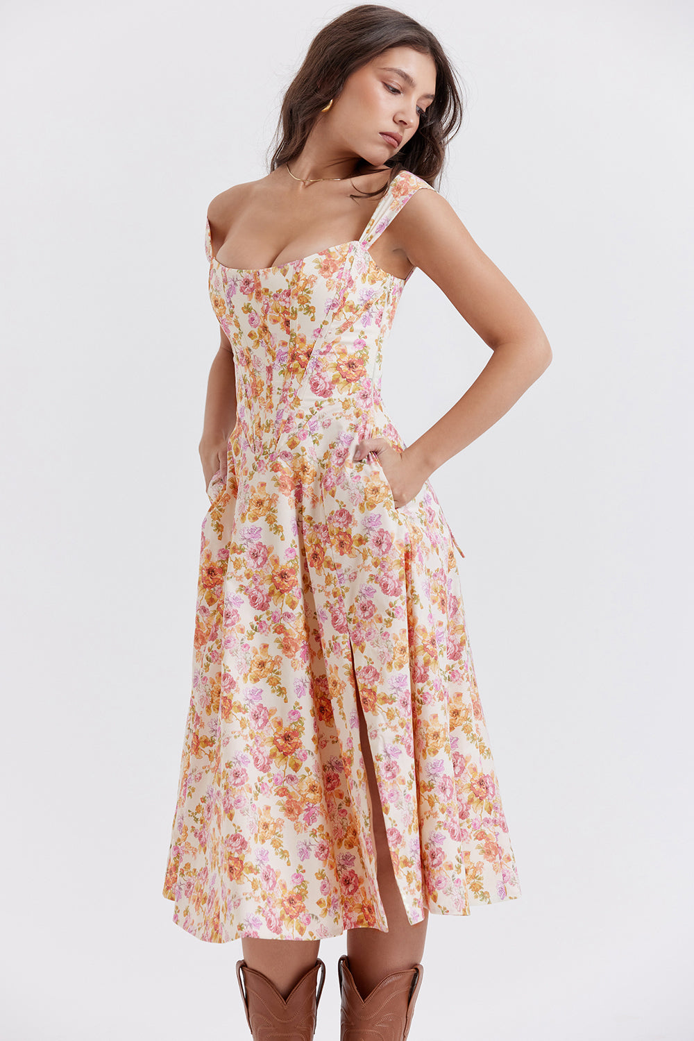 Robe longue à fleurs roses et oranges, style vintage, avec bretelles larges et poches, portée par une femme. Mode féminine élégante et estivale.