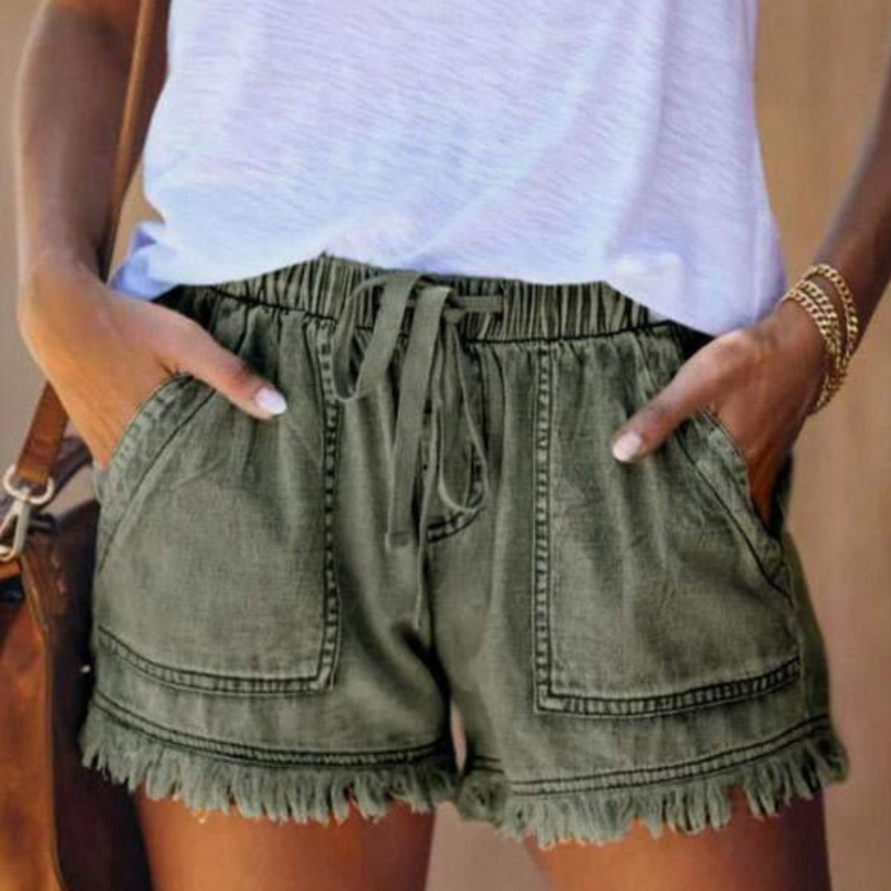 Short en jean vert kaki avec poches avant et ourlet à franges, porté avec un t-shirt blanc. Mode estivale décontractée pour femmes.