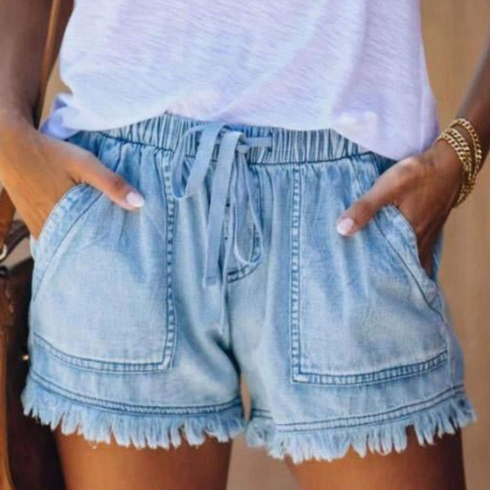 Short en jean bleu clair avec cordon de serrage, poches avant et ourlet à franges, porté avec un t-shirt blanc. Mode estivale décontractée.
