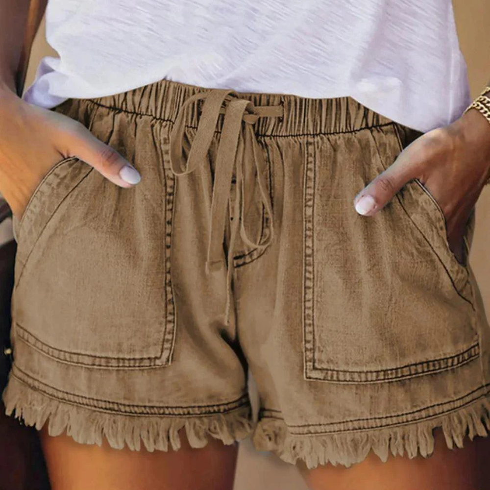Short en jean marron avec poches avant, taille élastique et ourlet à franges, porté avec un t-shirt blanc. Mode décontractée estivale pour femmes.