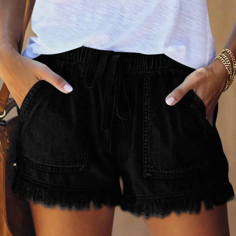 Short en jean noir pour femme avec poches, ceinture élastique et ourlet à franges, porté avec un t-shirt blanc. Mode estivale décontractée.
