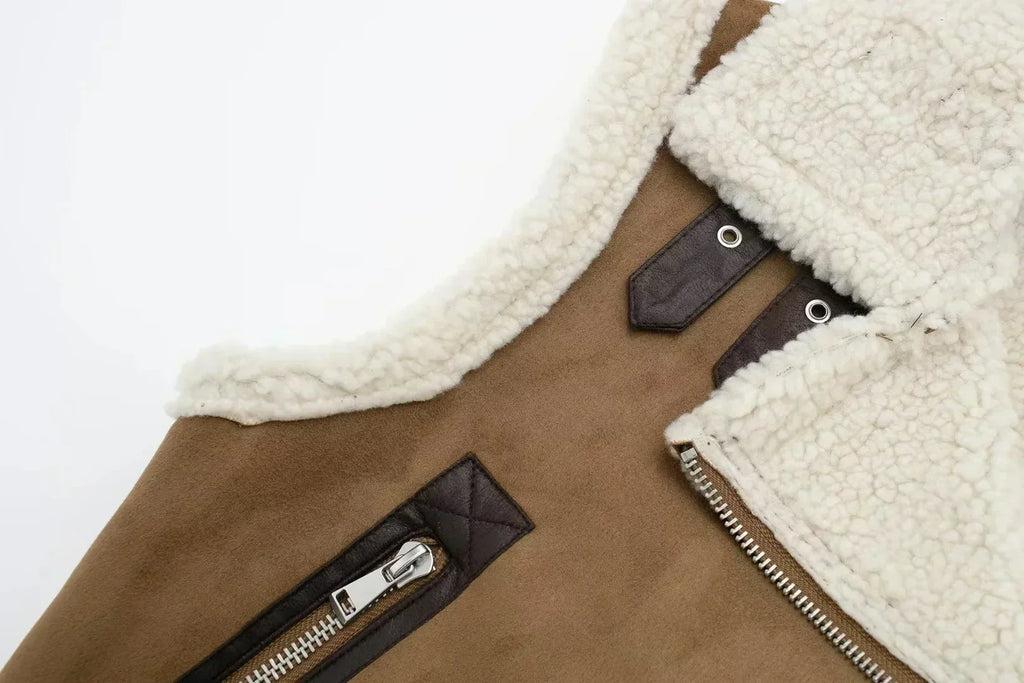 Veste en daim marron avec doublure en laine blanche, fermeture éclair argentée et détails en cuir noir. Mode hiver, style élégant et chaud.