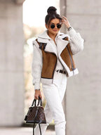 Femme élégante portant une veste en peau lainée marron, pull blanc, lunettes de soleil rondes et sac à main à carreaux, style automne chic.