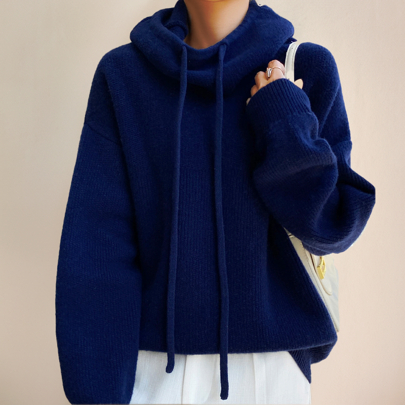 Pull-over bleu marine à col roulé avec cordons, porté par une personne tenant un sac blanc. Mode automne-hiver, style décontracté et élégant.
