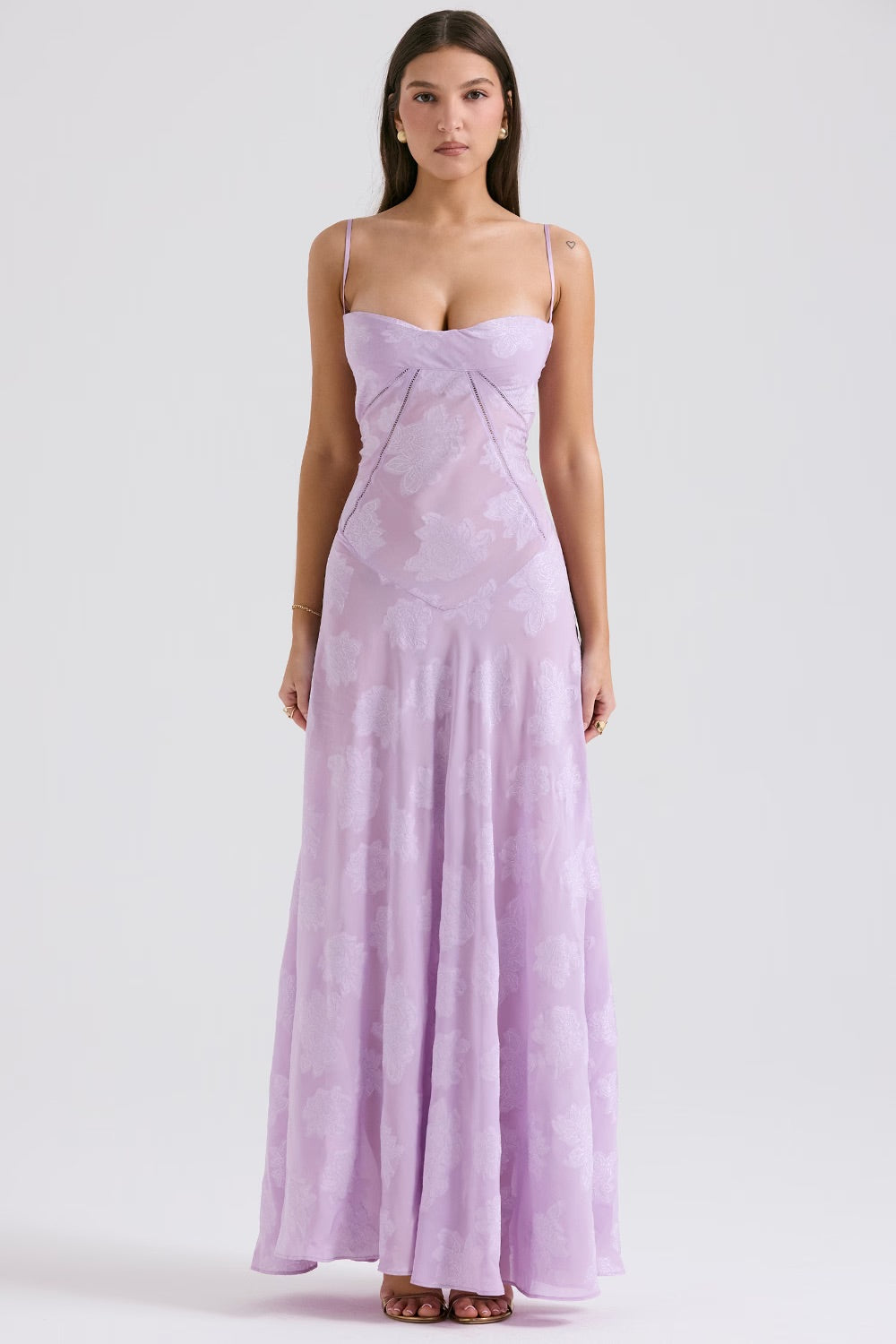 Robe longue lilas en dentelle florale, bretelles fines, décolleté en cœur, portée par une femme. Mode élégante, tenue de soirée chic.