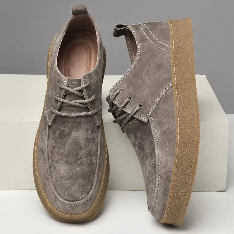 Chaussures en daim gris pour homme avec semelle en caoutchouc beige, style décontracté, lacets assortis, posées sur fond neutre.
