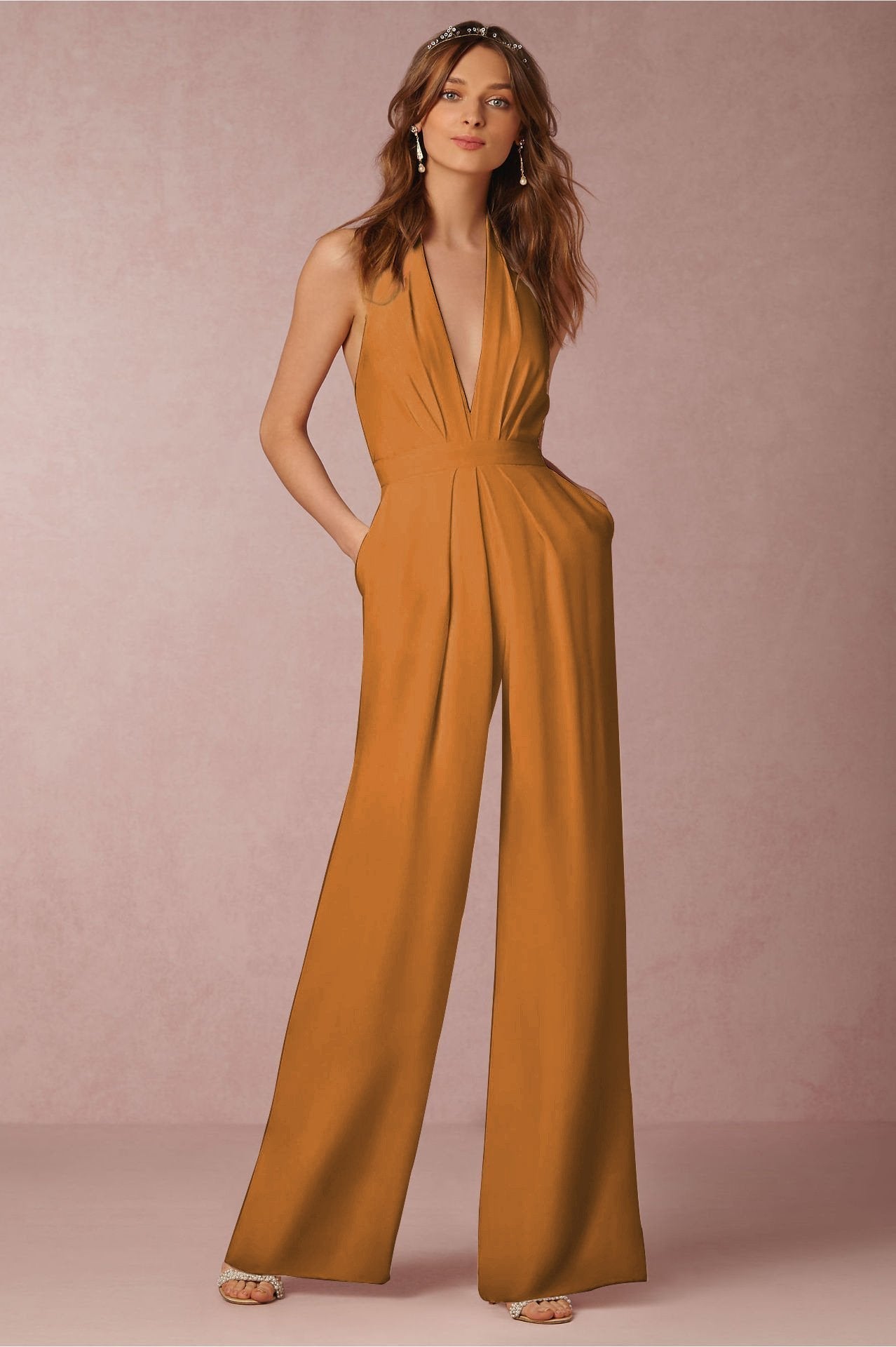 Femme portant une combinaison orange élégante avec décolleté plongeant, posant sur fond rose. Mode féminine, tenue chic, style moderne.