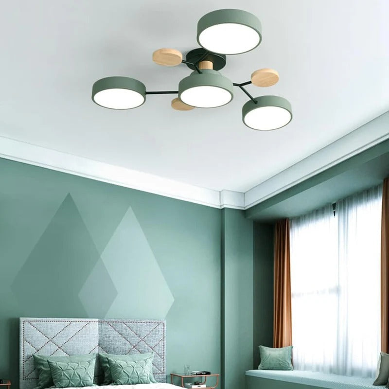 Plafonnier moderne à LED vert et bois dans une chambre élégante avec murs verts, lit avec coussins assortis et grandes fenêtres lumineuses.