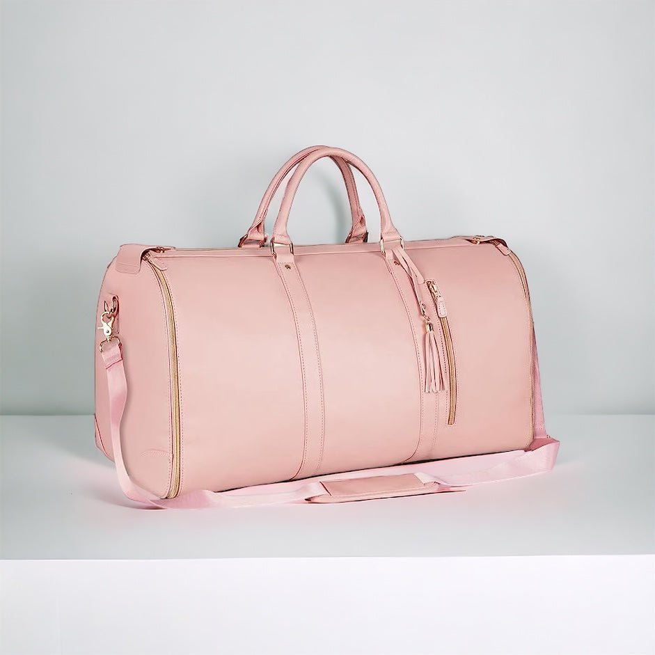 Sac de voyage rose en cuir, élégant et spacieux, avec bandoulière ajustable et fermetures éclair dorées, posé sur une surface blanche.