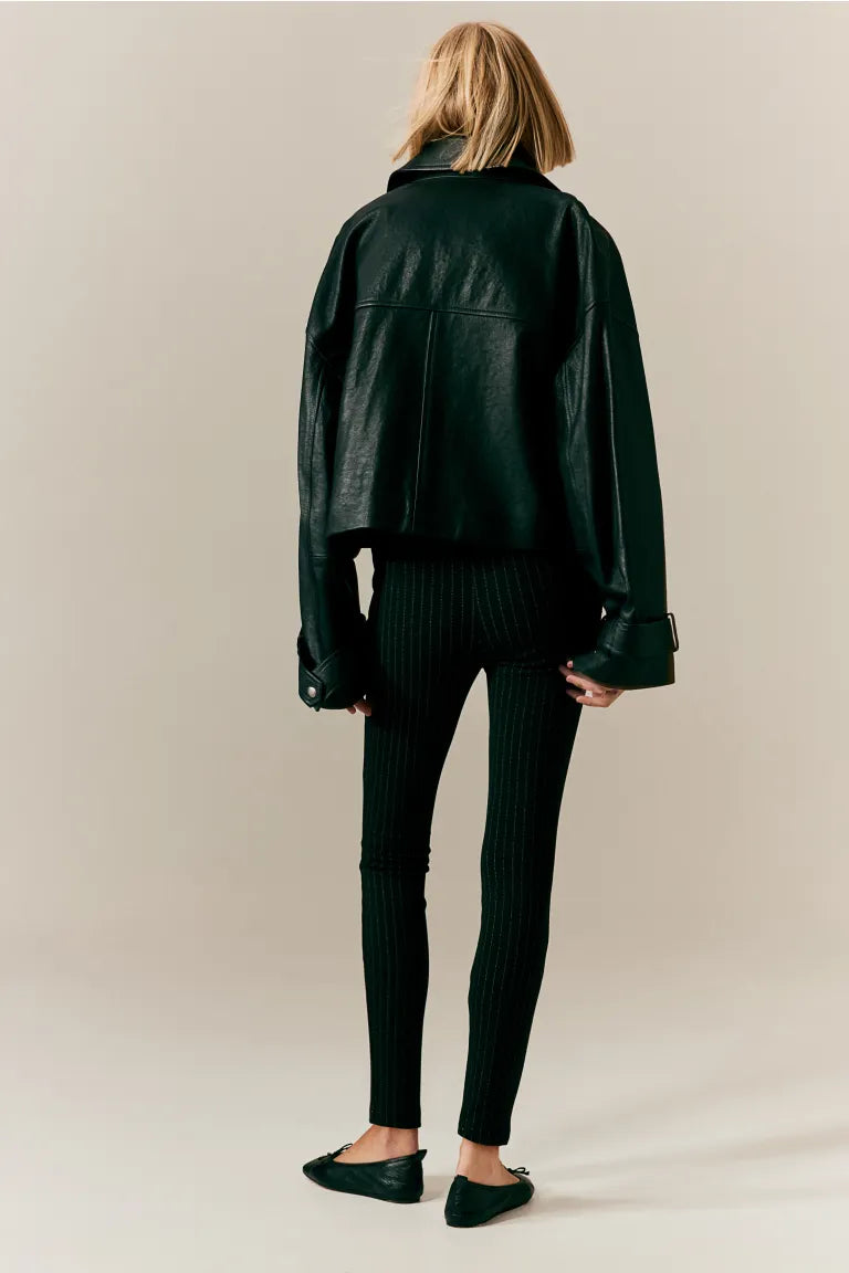 Femme de dos portant une veste en cuir noir oversize, leggings noirs côtelés et ballerines noires. Mode automne, style urbain chic.
