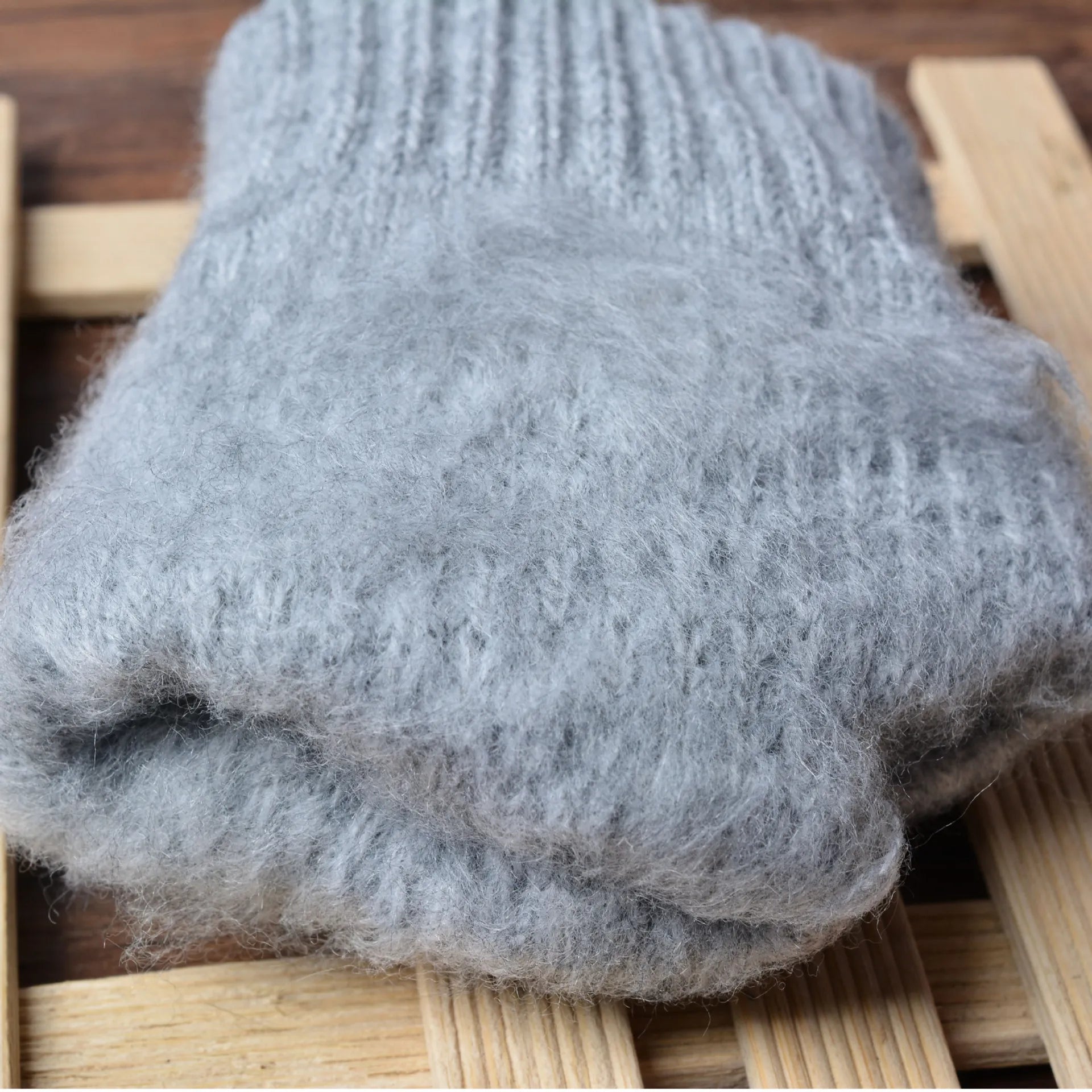 Gants en laine grise moelleuse posés sur une surface en bois, parfaits pour l'hiver. Accessoire chaud, doux et confortable pour le froid.