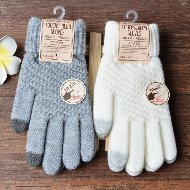 Gants tactiles gris et blancs en tricot, étiquetés pour écran tactile, posés sur une table en bois avec une fleur blanche à côté.