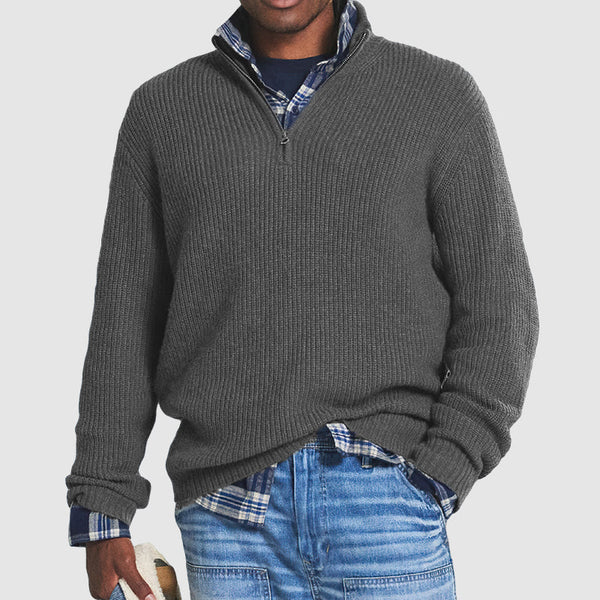 Homme portant un pull gris à col zippé sur une chemise à carreaux bleue, avec un jean décontracté. Mode masculine automne-hiver, style décontracté.
