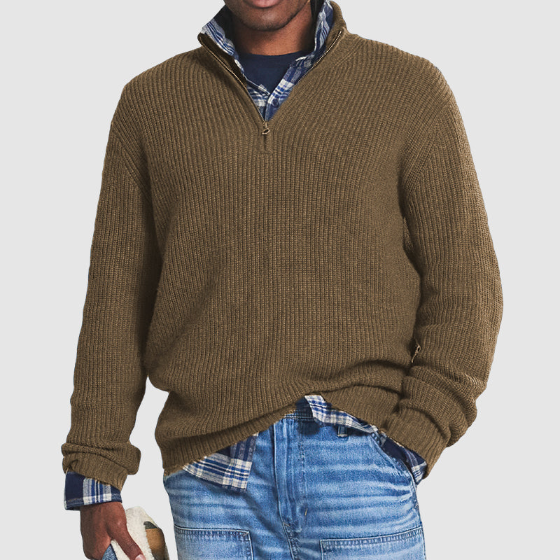 Homme portant un pull en maille marron avec fermeture éclair, chemise à carreaux bleue et jean décontracté. Mode automne-hiver, style décontracté.