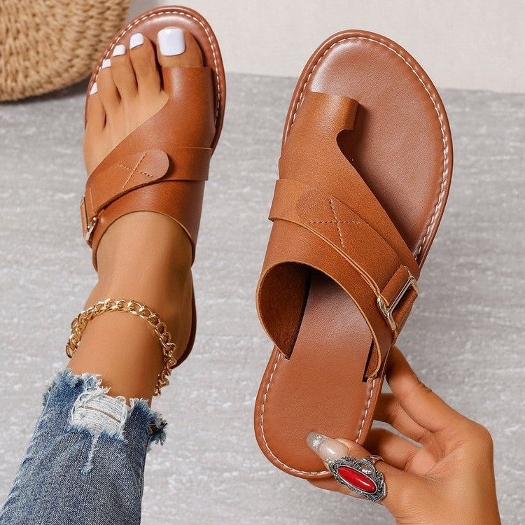 Sandales en cuir marron pour femme avec boucle, portées avec un jean déchiré et un bracelet doré. Mode estivale, chaussures confortables.