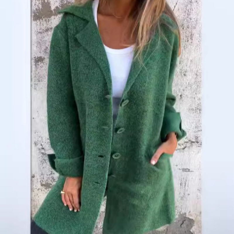 Femme portant un manteau vert en laine, style décontracté, avec boutons et poches, sur fond de mur texturé. Mode automne-hiver tendance.