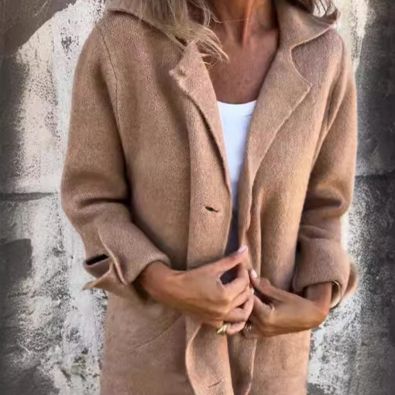 Femme portant un manteau en laine beige, manches retroussées, sur fond de mur texturé. Mode automne, style décontracté, élégance moderne.