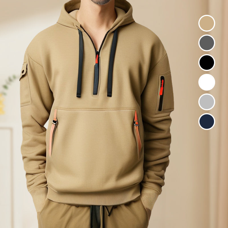 Homme portant un sweat à capuche beige avec poches zippées et cordons noirs, style décontracté. Palette de couleurs neutres en arrière-plan.