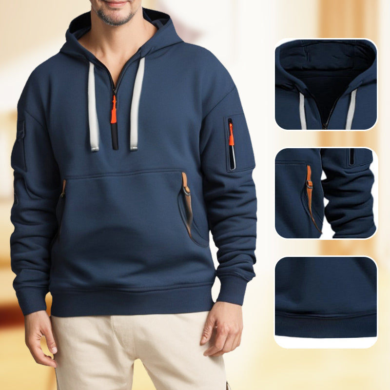 Homme portant un sweat à capuche bleu marine avec poches zippées et détails orange, style décontracté. Mode masculine, vêtements tendance.