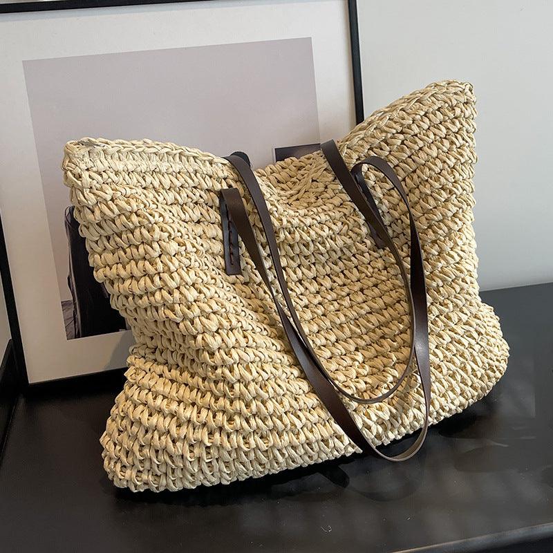 Sac cabas en paille tressée avec anses en cuir marron, posé sur une table noire devant un cadre. Accessoire mode estival, tendance et pratique.
