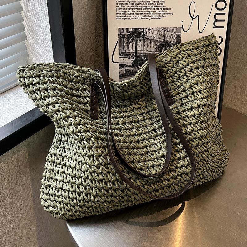 Sac en paille tressée vert olive avec anses en cuir marron, posé sur une table près d'une fenêtre. Accessoire mode tendance et estival.