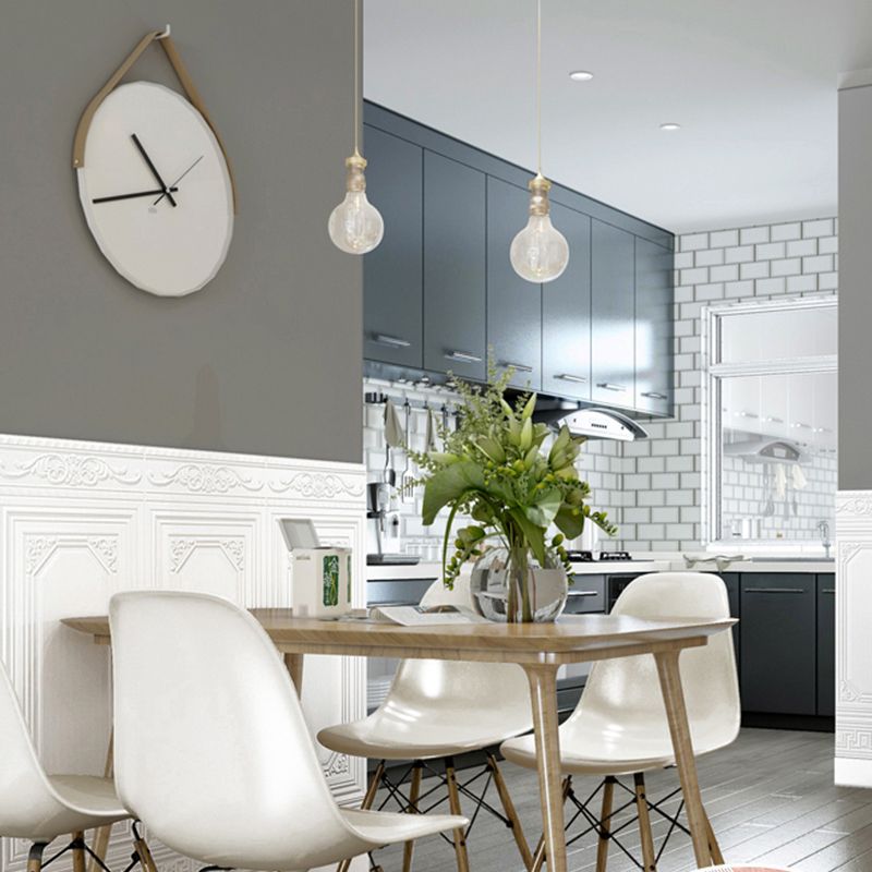 Salle à manger moderne avec table en bois, chaises blanches, horloge murale design, cuisine grise en arrière-plan, et suspension lumineuse.