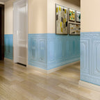 Couloir intérieur avec lambris bleu, sol en bois clair, porte blanche et tableaux modernes. Décoration murale élégante et contemporaine.