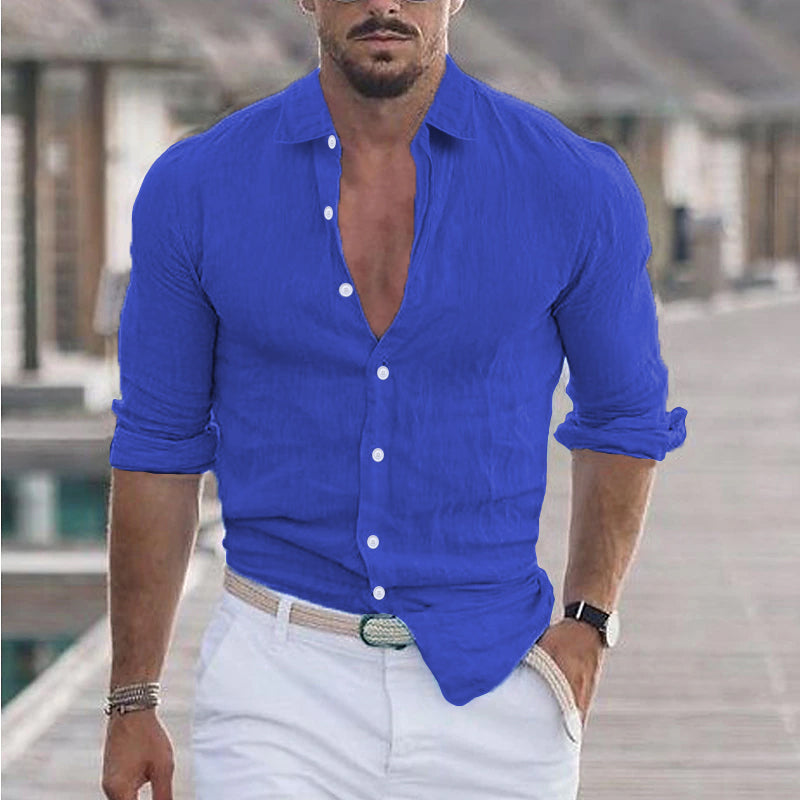 Homme portant une chemise bleue élégante, manches retroussées, sur une promenade en bois. Mode masculine, style décontracté chic, été.