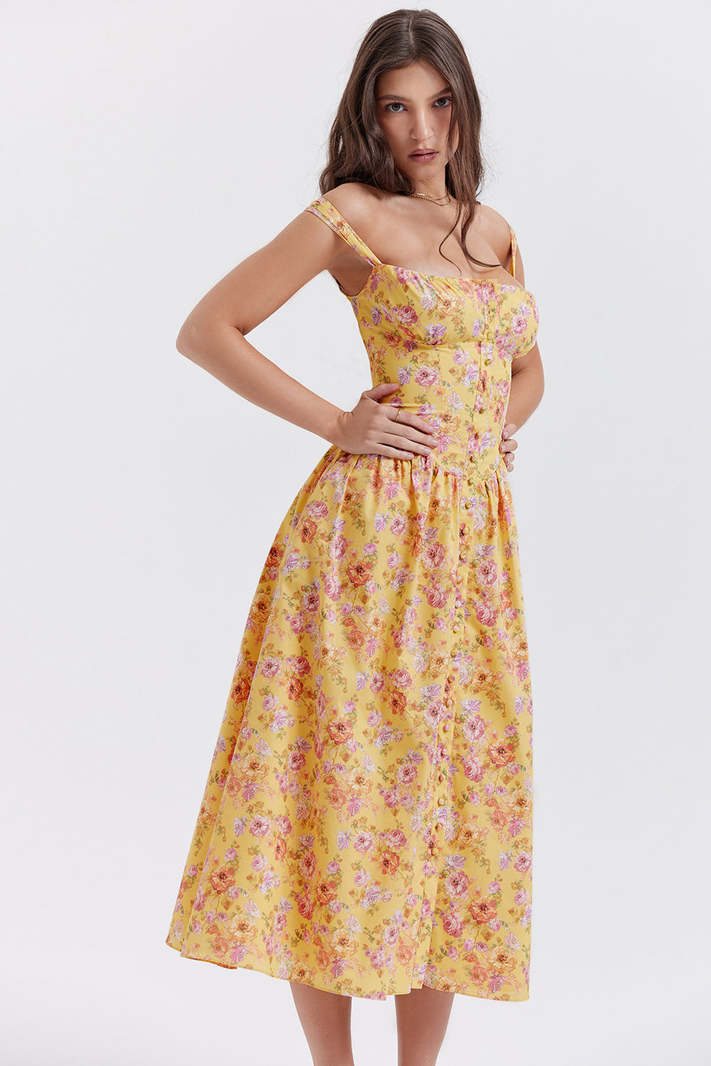 Robe longue jaune à fleurs roses portée par une femme, style été, bretelles fines, fond blanc. Mode féminine, tendance estivale, élégance florale.